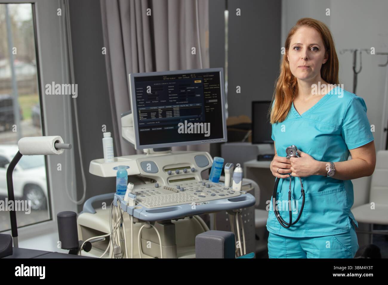 Ritratto di donna medico o ecografo in scrub in piedi nella moderna sala diagnostica a ultrasuoni con attrezzature mediche e stetoscopio Foto Stock