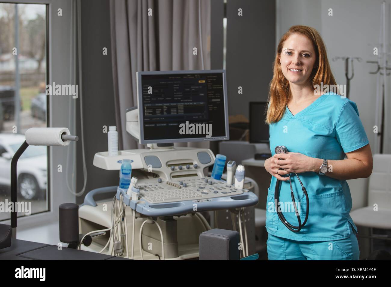 Ritratto di donna medico o ecografo in scrub in piedi nella moderna sala diagnostica a ultrasuoni con attrezzature mediche e stetoscopio Foto Stock