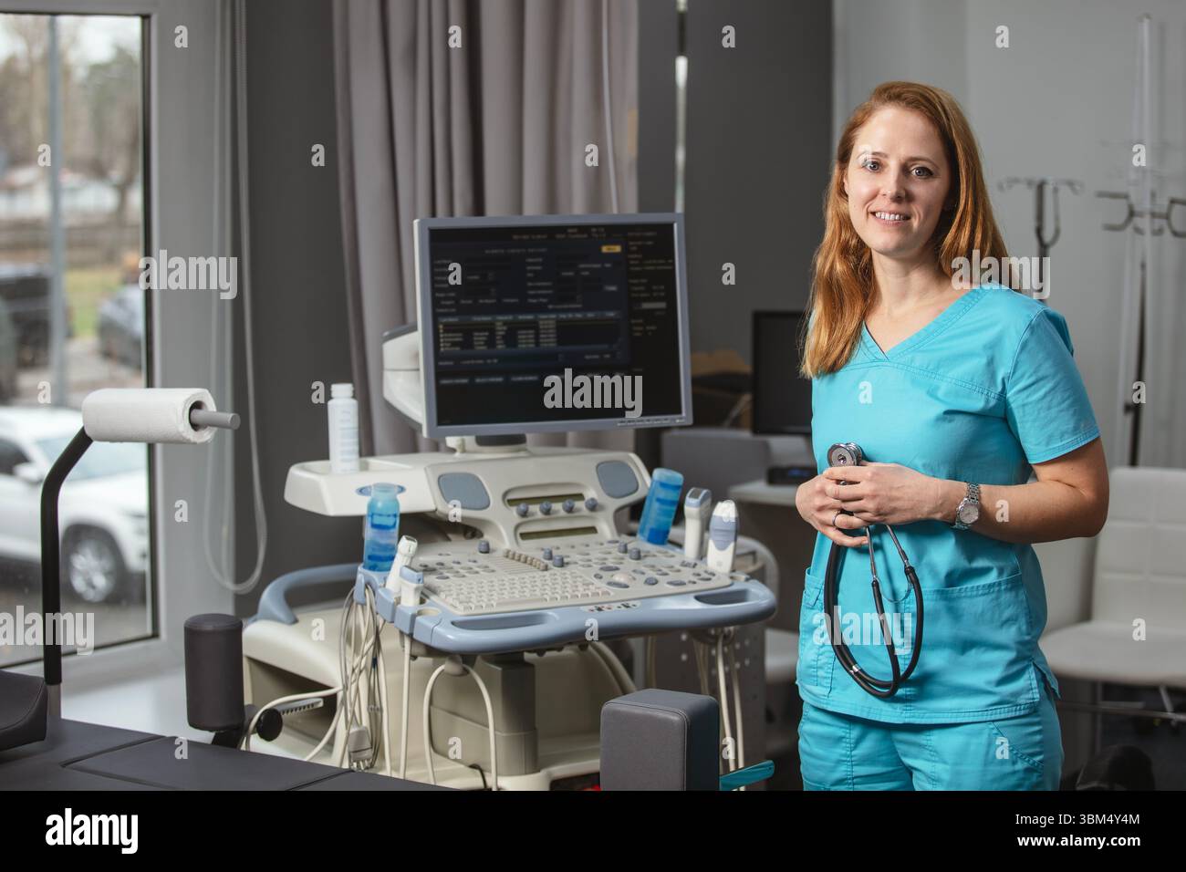 Ritratto di donna medico o ecografo in scrub in piedi nella moderna sala diagnostica a ultrasuoni con attrezzature mediche e stetoscopio Foto Stock