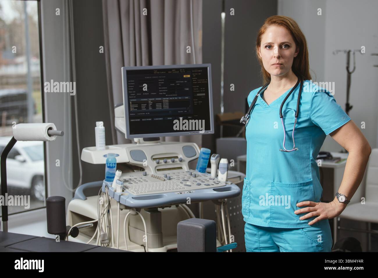 Ritratto di donna medico o ecografo in scrub in piedi nella moderna sala diagnostica a ultrasuoni con attrezzature mediche e stetoscopio Foto Stock