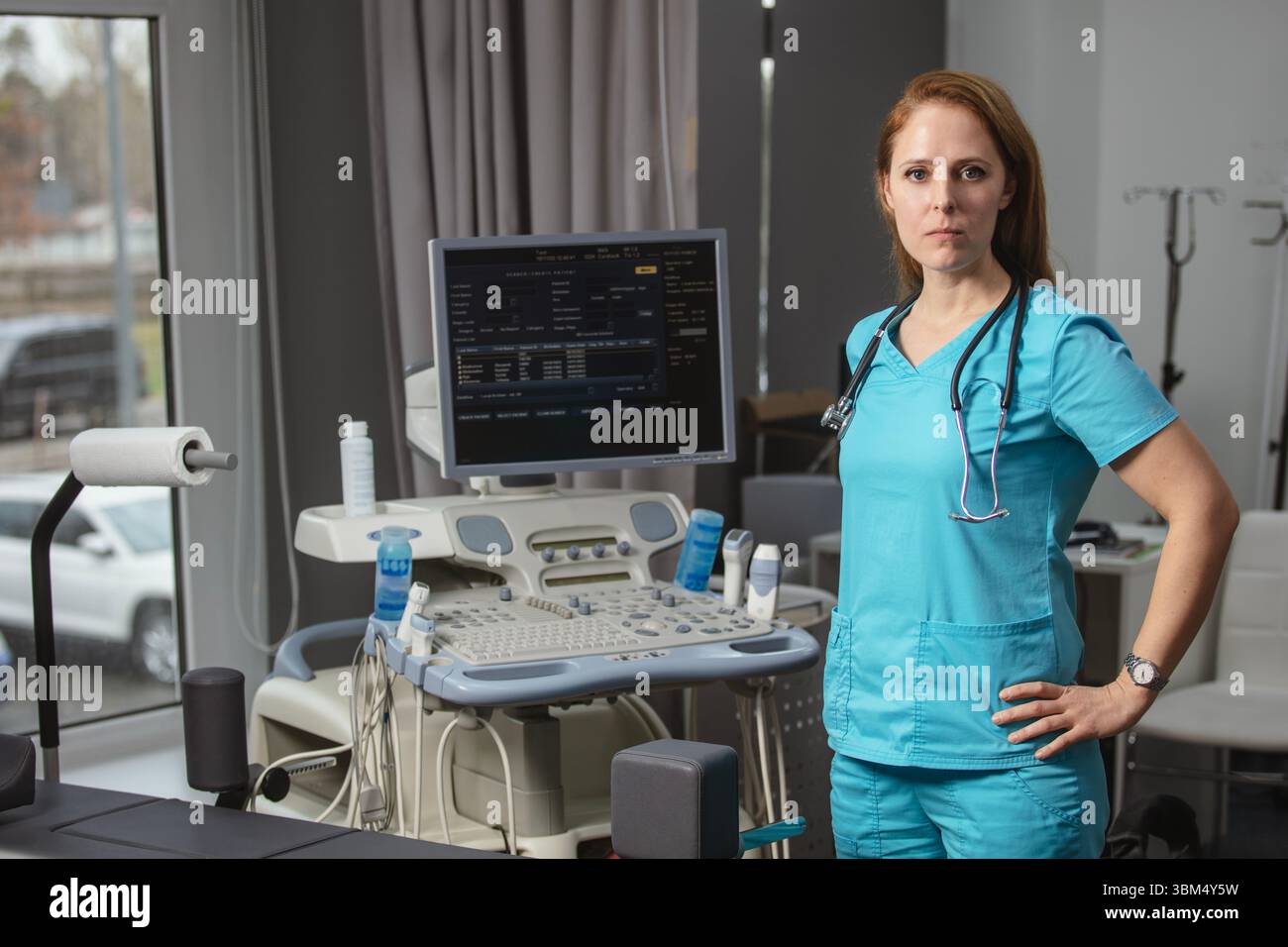 Ritratto di donna medico o ecografo in scrub in piedi nella moderna sala diagnostica a ultrasuoni con attrezzature mediche e stetoscopio Foto Stock