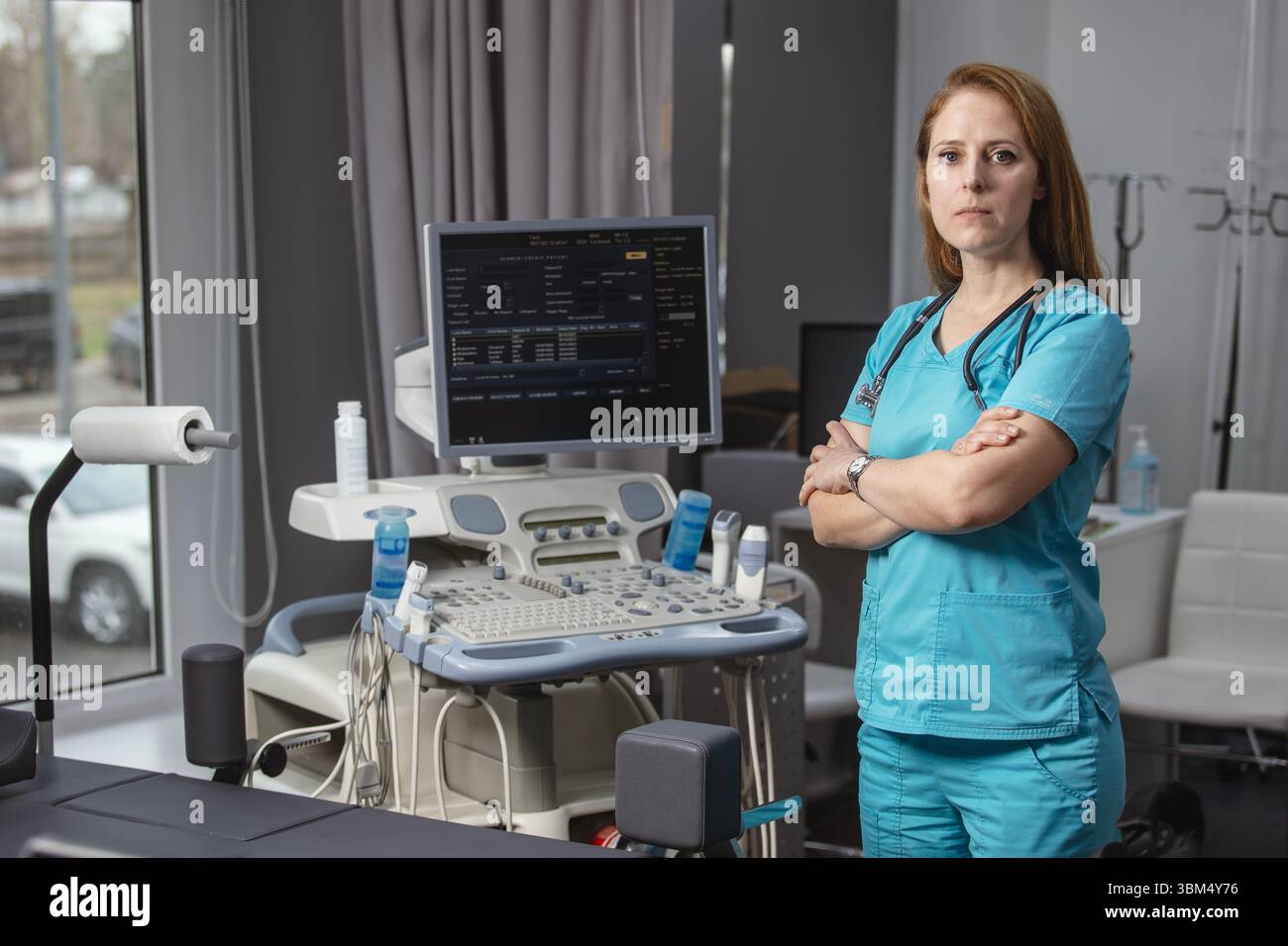 Ritratto di donna medico o ecografo in scrub in piedi nella moderna sala diagnostica a ultrasuoni con attrezzature mediche e stetoscopio Foto Stock