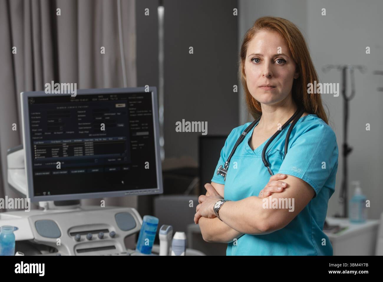 Ritratto di donna medico o ecografo in scrub in piedi nella moderna sala diagnostica a ultrasuoni con attrezzature mediche e stetoscopio Foto Stock