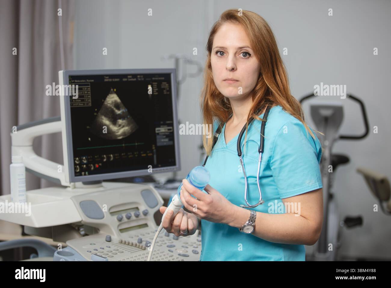 Ritratto di donna medico o ecografo in scrub in piedi nella moderna sala diagnostica a ultrasuoni con attrezzature mediche e stetoscopio Foto Stock