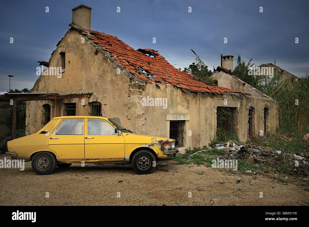 Una vecchia macchina gialla parcheggiata davanti ad una casa abbandonata in rovina. Foto Stock