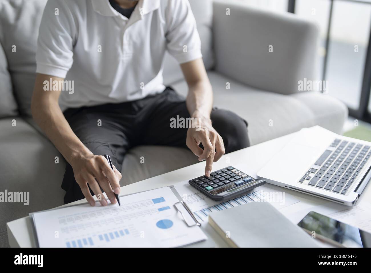 L'uomo calcola le finanze la casa paga le bollette le tasse sul telefono cellulare e calcolatrice finanziaria a casa Foto Stock