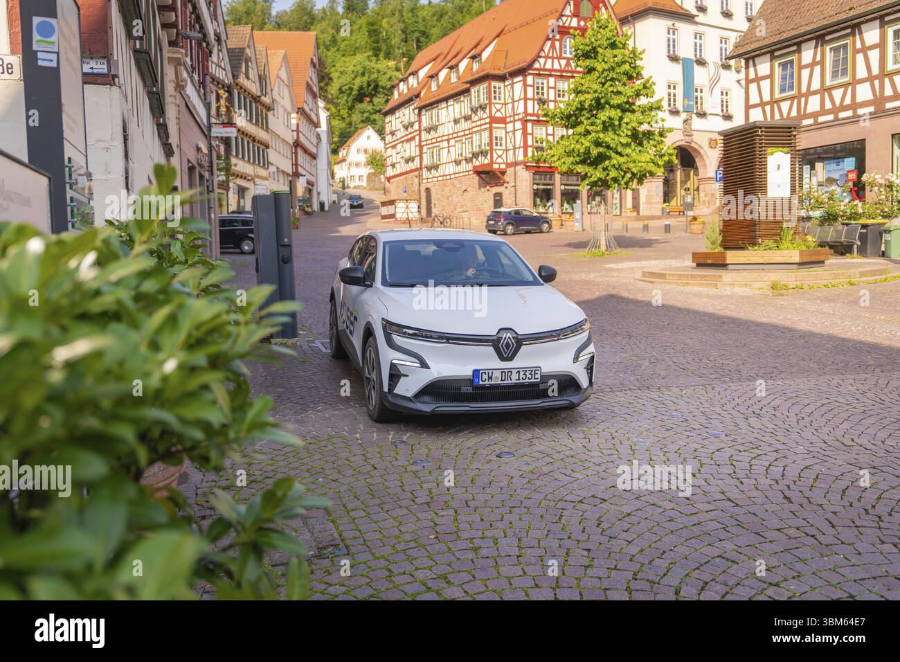 Un'auto su una strada acciottolata circondata da tradizionali case in legno e vegetazione verde, cervi e, car sharing, auto elettrica, Calw, foresta Nera Foto Stock