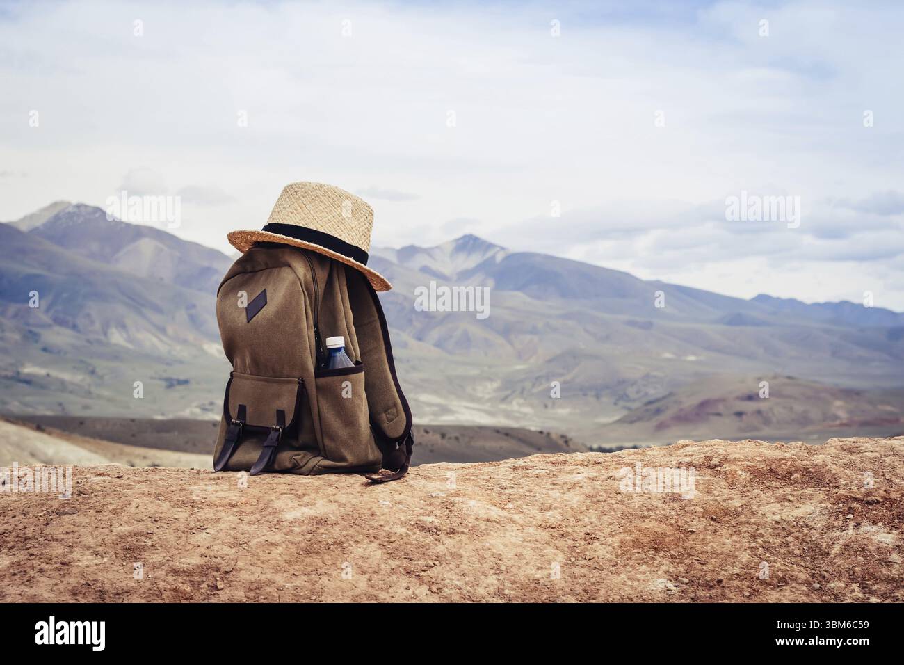 Zaino beige, bottiglia d'acqua e cappello di paglia sulle colline in montagna. Concetto di marcia attiva Foto Stock