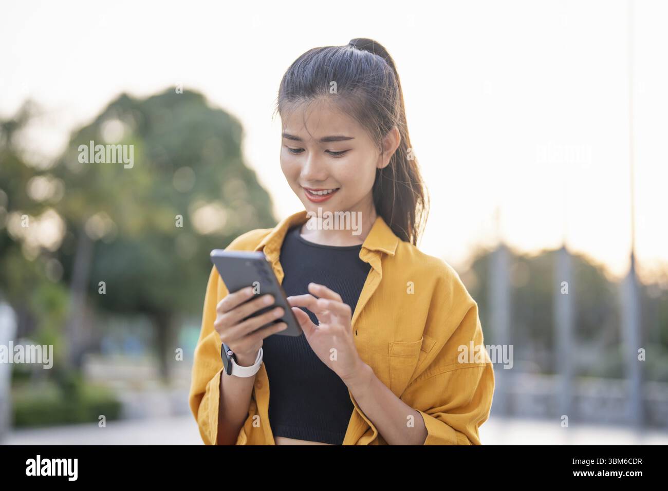 Sorridente giovane donna asiatica che usa lo smartphone in città controllando app mobili all'aperto Foto Stock