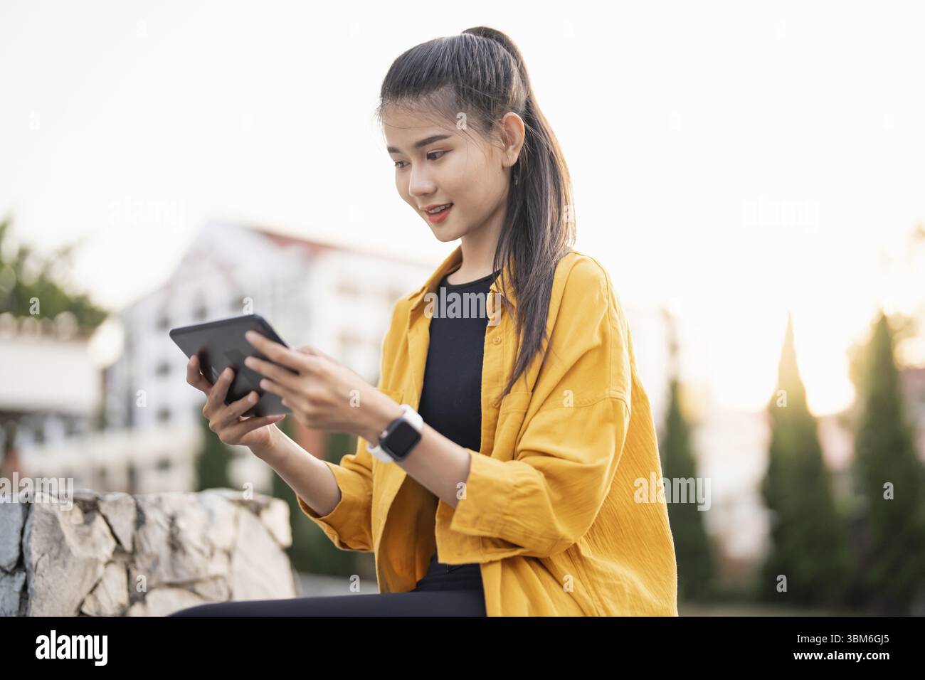 Sorridente giovane donna asiatica che usa un tablet digitale in città Foto Stock