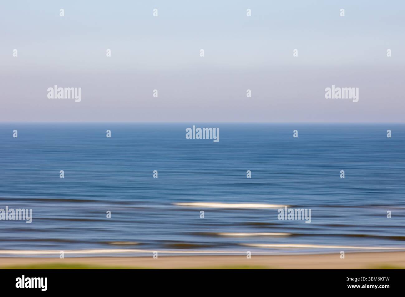 I tenui colori pastello si fondono perfettamente in una scena oceanica sfocata, creando linee orizzontali astratte mentre le onde rotolano dolcemente verso la riva al crepuscolo Foto Stock
