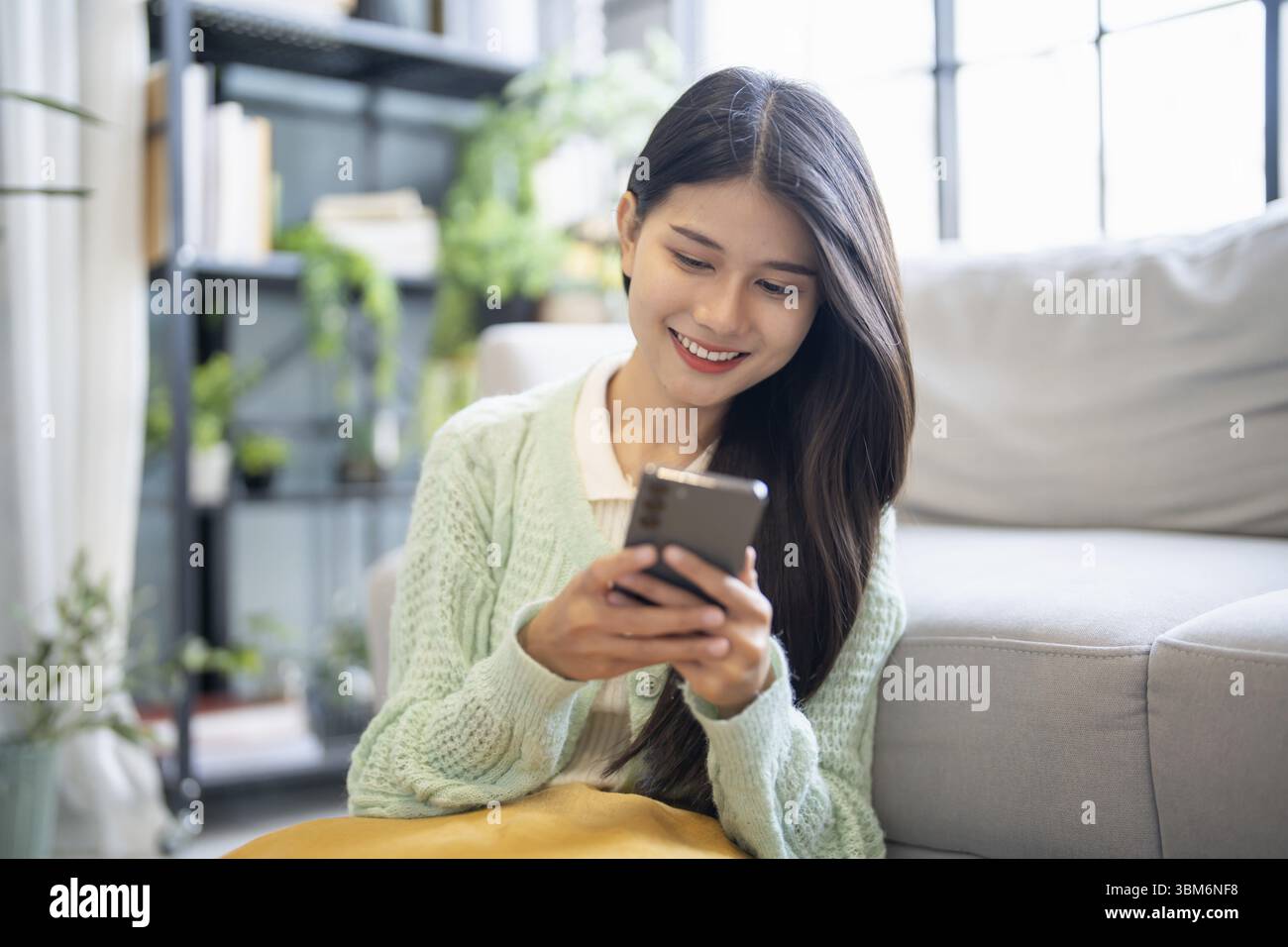 Donna asiatica che utilizza l'assistente vocale sullo smartphone a casa conversazione con assistente online chat vocale bot conversazionale ai tecnologie moderne Foto Stock