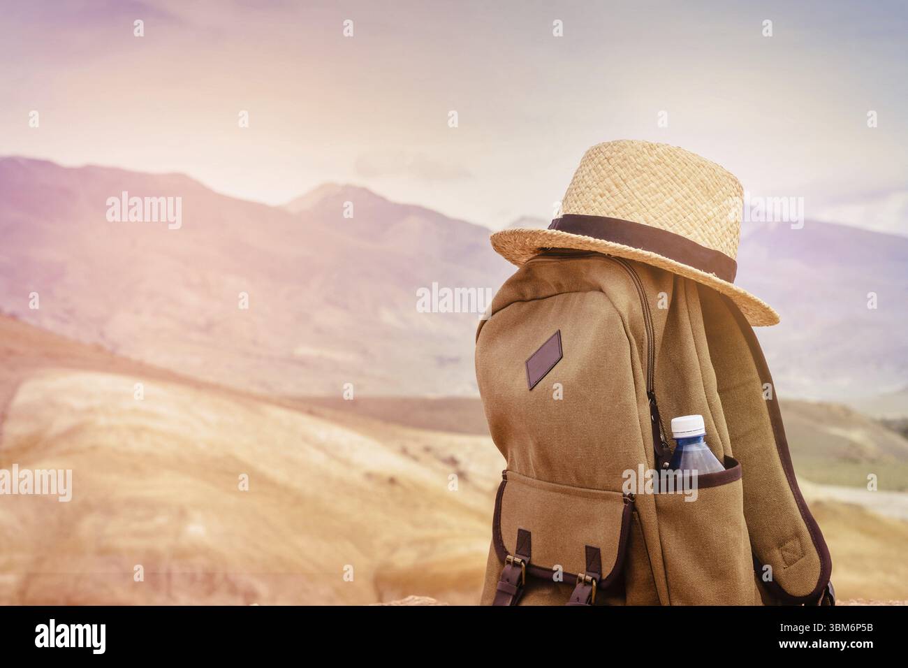 Zaino beige, bottiglia d'acqua e cappello di paglia in cima alla montagna. Concetto di marcia attiva. Tonificante alba Foto Stock