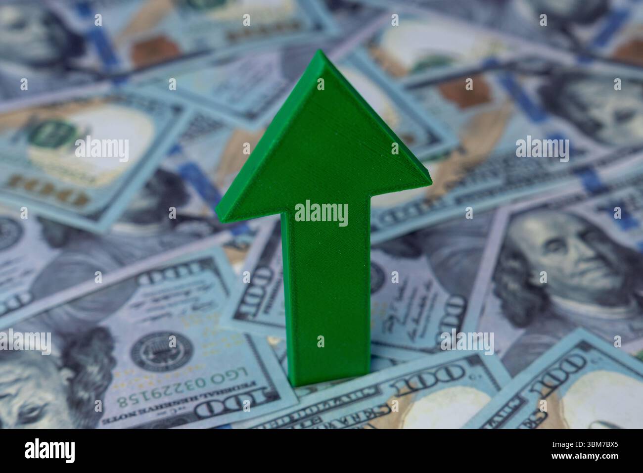 Una freccia verde punta verso l'alto sullo sfondo di banconote sparse da cento dollari. Crescita finanziaria, prosperità economica Foto Stock