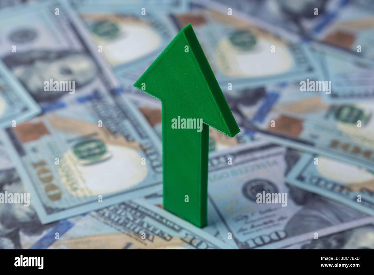 Una freccia verde punta verso l'alto sullo sfondo di banconote sparse da cento dollari. Crescita finanziaria, prosperità economica Foto Stock