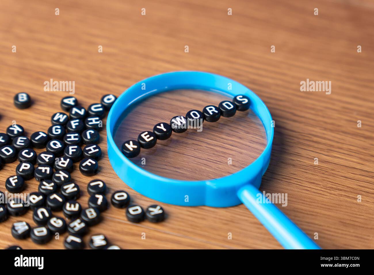 Una lente d'ingrandimento blu con perline alfabetiche che esprimono PAROLE CHIAVE. Ricerca, ottimizzazione, scoperta, SEO, dati, e contenuti online. Foto Stock