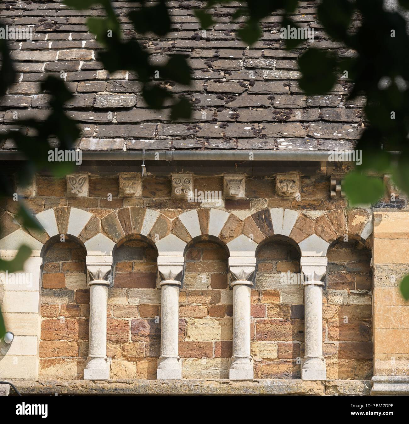 Archi a sezione tonda decorativi e teste su una parete esterna presso la chiesa cristiana di St Peter's norman costruita a Northampton, Inghilterra. Foto Stock