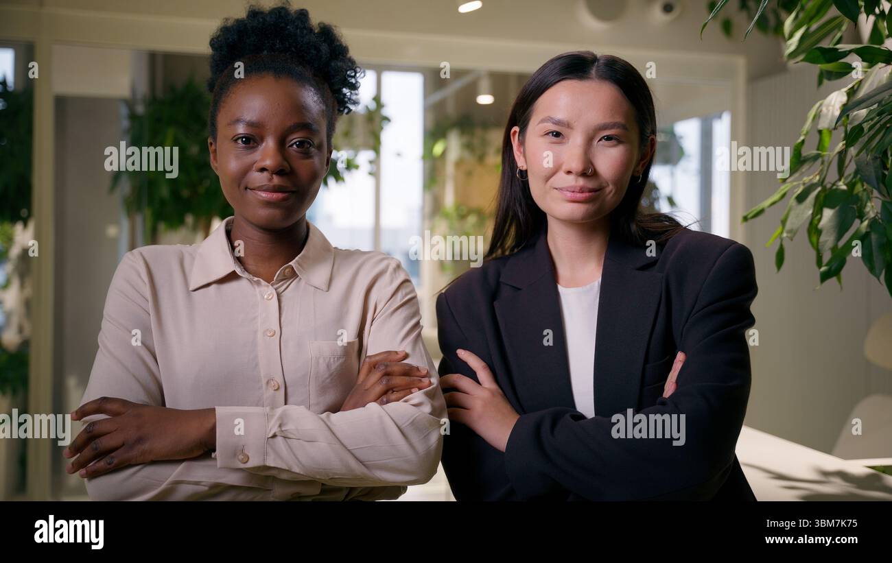 Due donne d'affari fiduciose multirazziali diverse ragazze africane asiatiche ritratti donne in ufficio che posano insieme armi incrociate affari cinesi americani Foto Stock