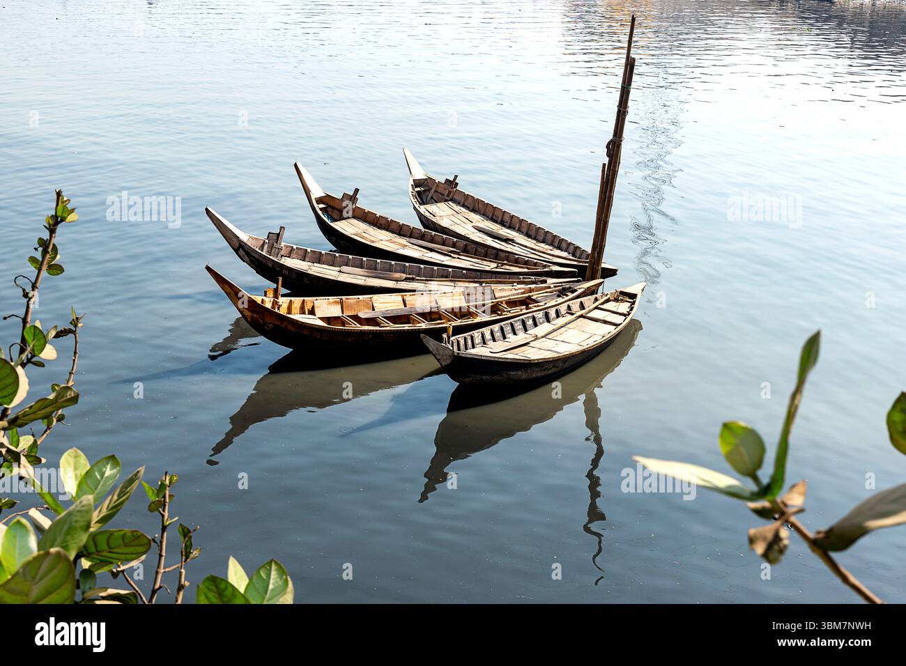 Diverse barche tradizionali in legno galleggiano dolcemente sulle acque calme, i loro riflessi scintillano alla luce del sole. Foto Stock