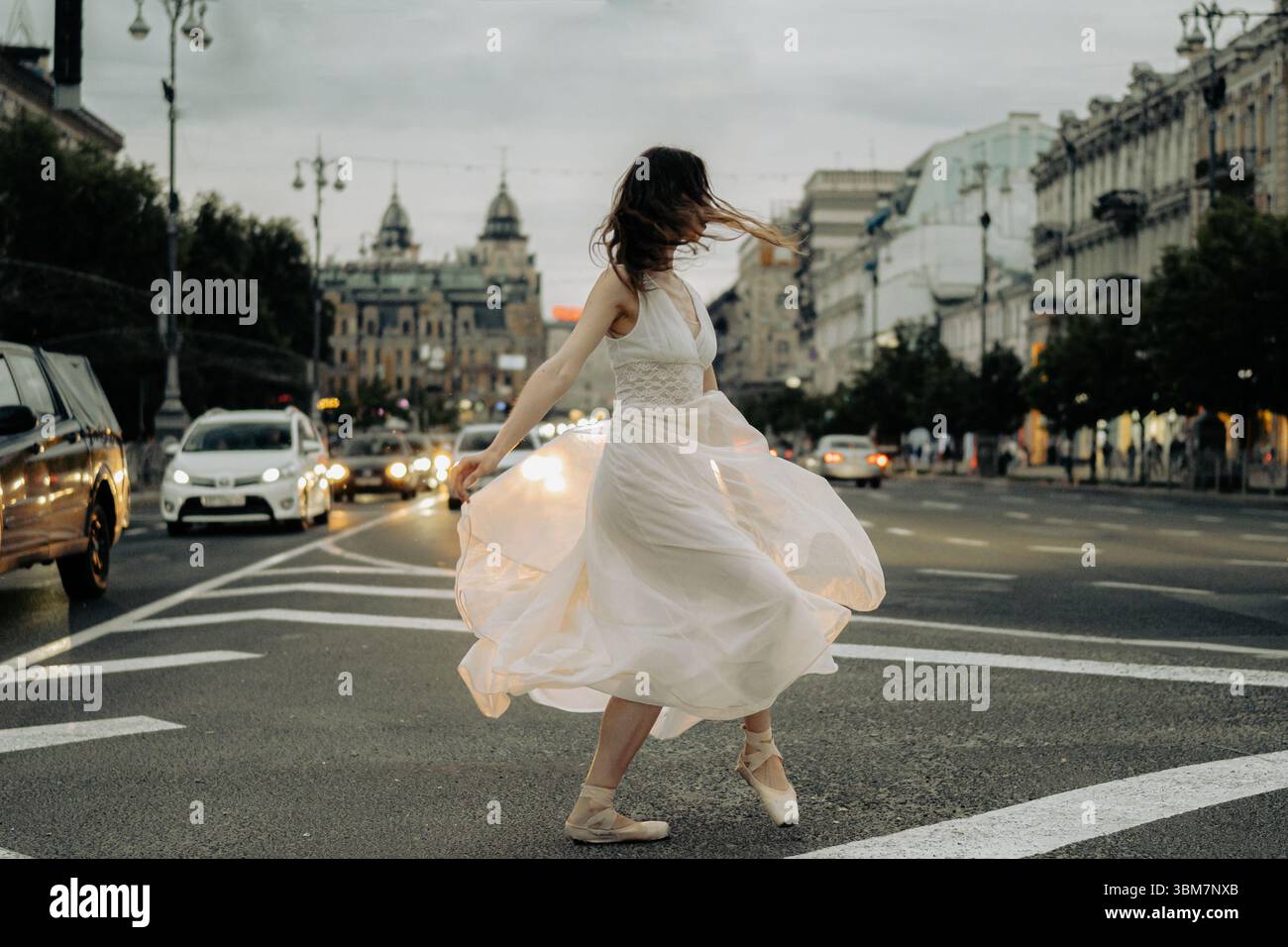 Una donna in un abito che scorre danzerà graziosamente nel mezzo di una strada della città, portando movimento e vita all'ambiente urbano. 18 maggio 2024, Kiev, Khre Foto Stock