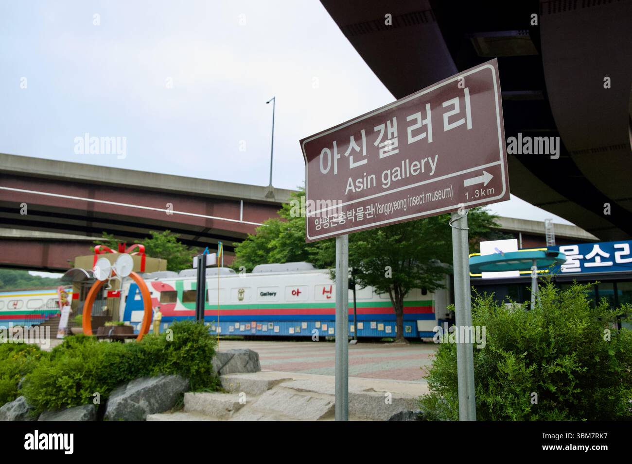 Contea di Yangpyeong, Corea del Sud - 19 maggio 2025: Un cartello stradale marrone punta a 1,3 km dalla Galleria ASIN presso la stazione ferroviaria di ASIN, sotto un'overpa Foto Stock