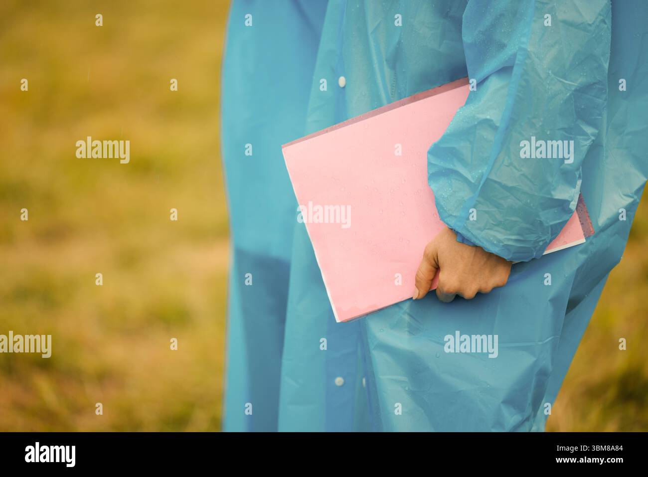 Persona in impermeabile con una cartellina rosa ricoperta di gocce di pioggia. Colori brillanti e texture bagnata Foto Stock