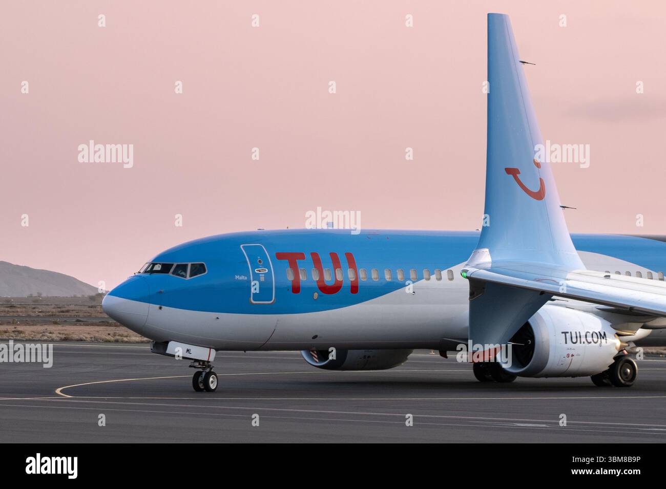 Aereo TUI sull'asfalto sotto un cielo di colore rosa, con la sua livrea blu e bianca e il suo logo. Foto Stock