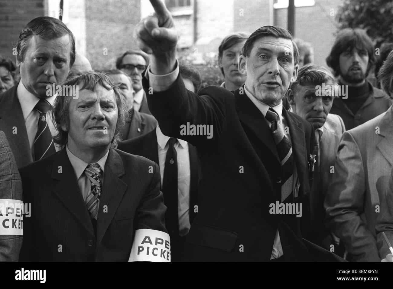 Grunwick strike picket line, Eric Clarke (a sinistra con cravatta). Presidente della National Union of Mineworkers e Presidente dell'area scozzese del NUM in seguito deputato laburista per Midlothian (1992-2001). Un funzionario Apex. Mick (Michael) McGahey (1925 – 1999) è stato un politico scozzese, leader dei minatori e comunista. Con la mano alzata e puntando (a destra) lo sciopero di Grunwick e la disputa industriale. Willesden, Londra, Inghilterra anni '1977 1970 UK HOMER SYKES Foto Stock
