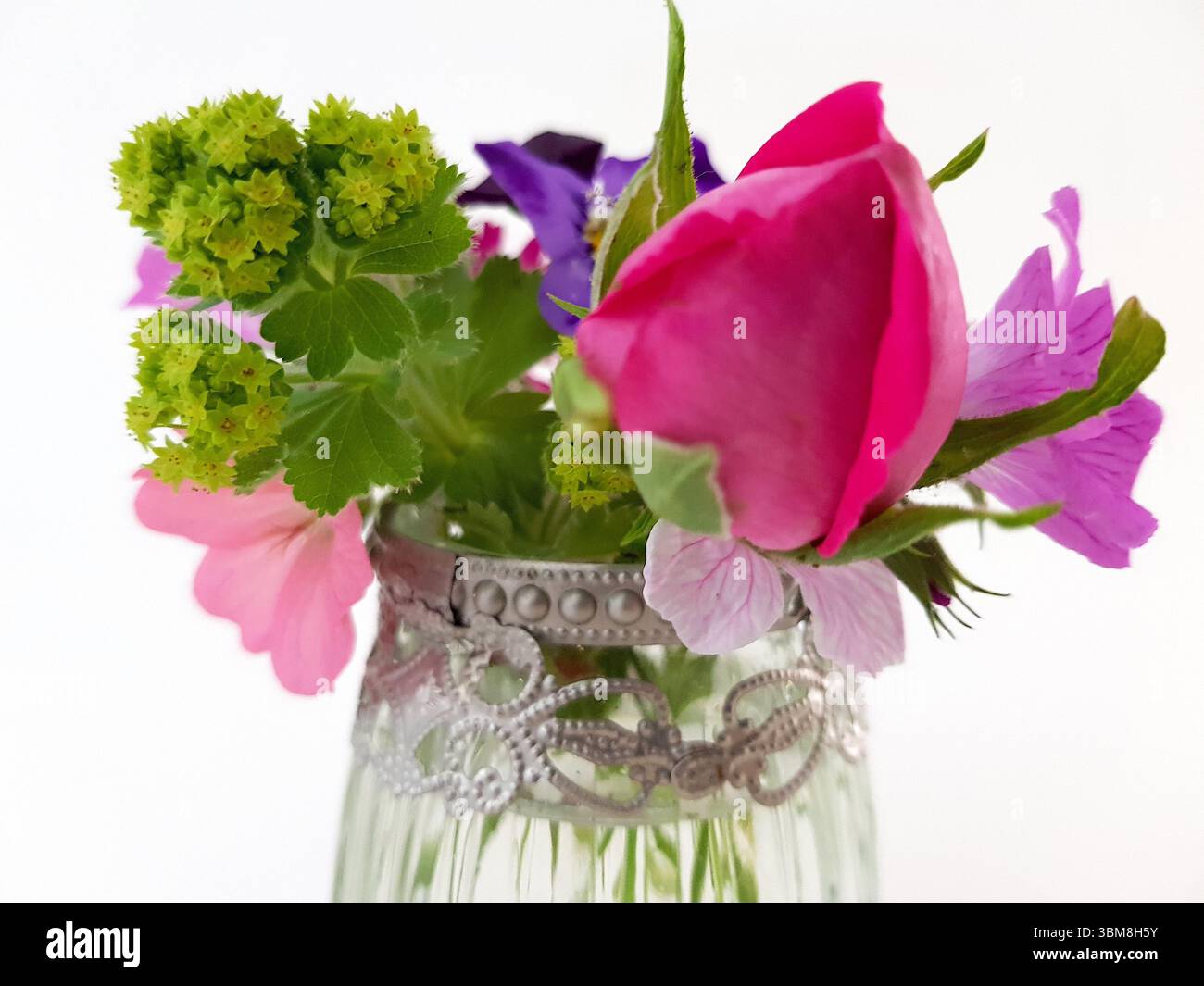 Un vaso decorativo in vetro con un'esposizione di fiori estivi colorati su sfondo bianco. Foto Stock
