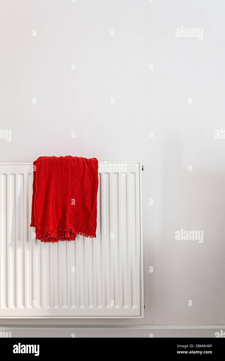 Sciarpa di pashmina rossa appesa ordinatamente su un radiatore bianco in una camera luminosa e moderna Foto Stock