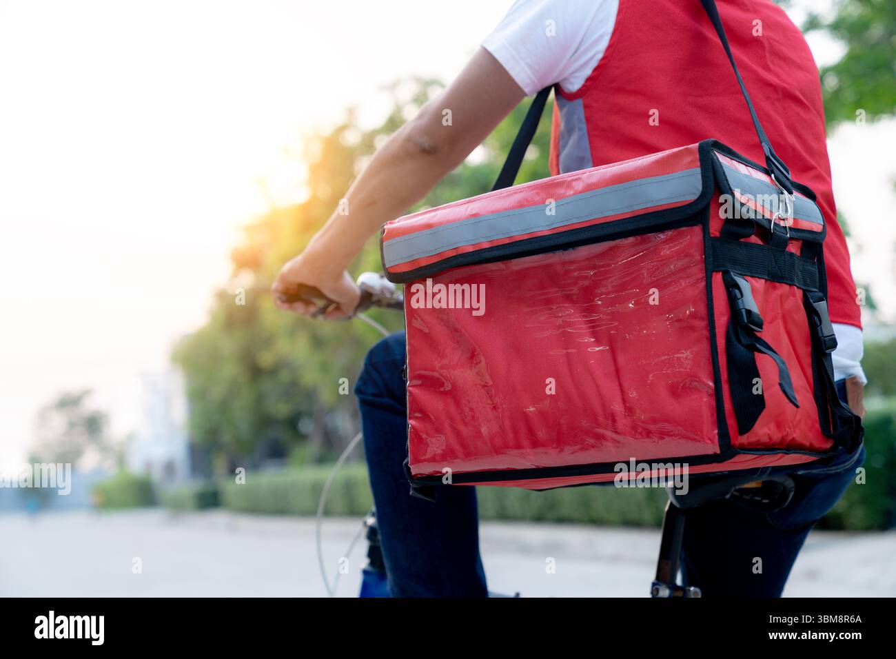 Giovane ciclista di consegna maschile che lavora part-time, percorrendo le strade della città con lo zaino. Foto Stock