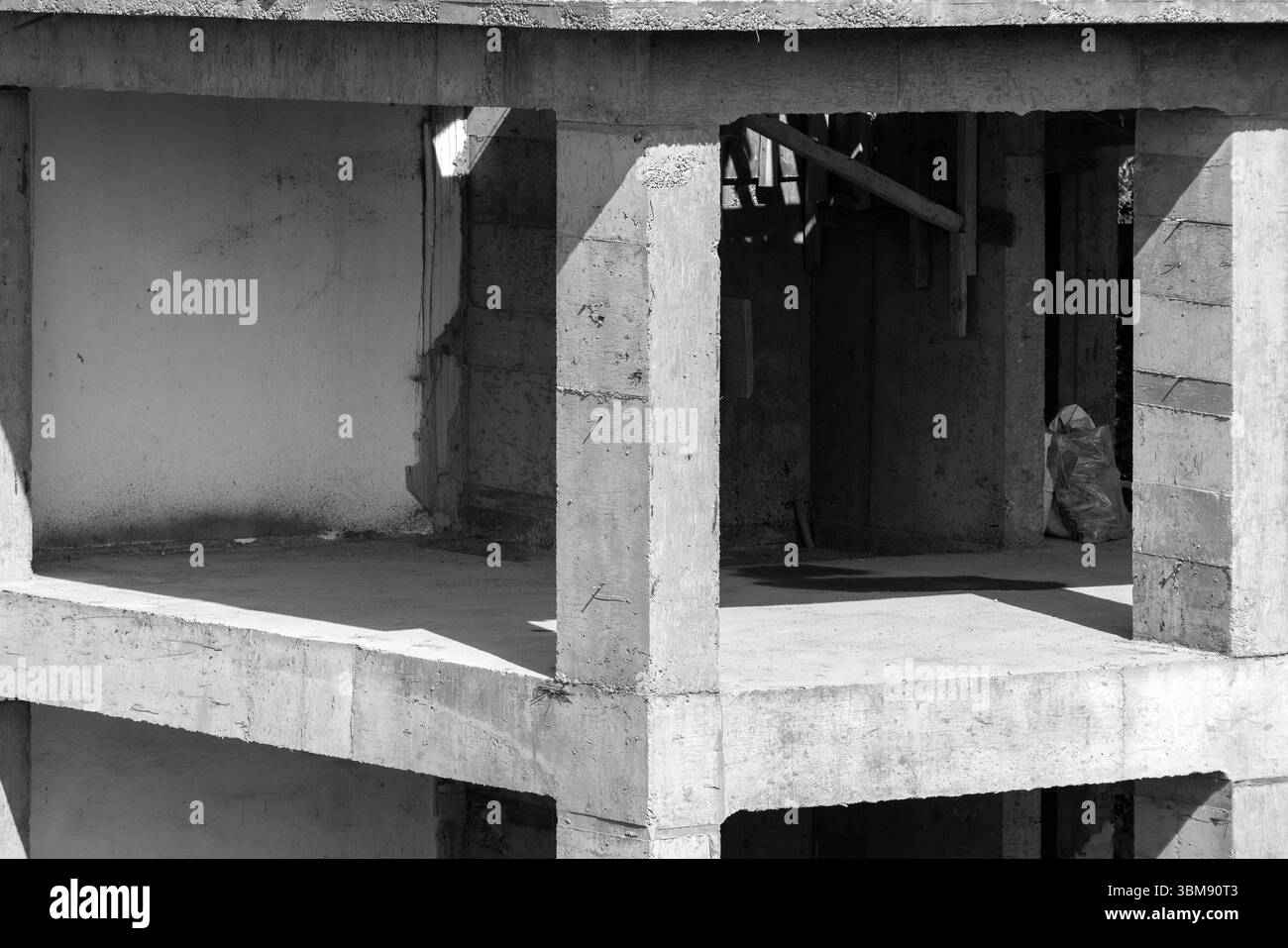 Una fotografia in scala di grigi che mostra un edificio incompleto con struttura in cemento armato. L'interazione di luci e ombre mette in risalto l'architetto Foto Stock