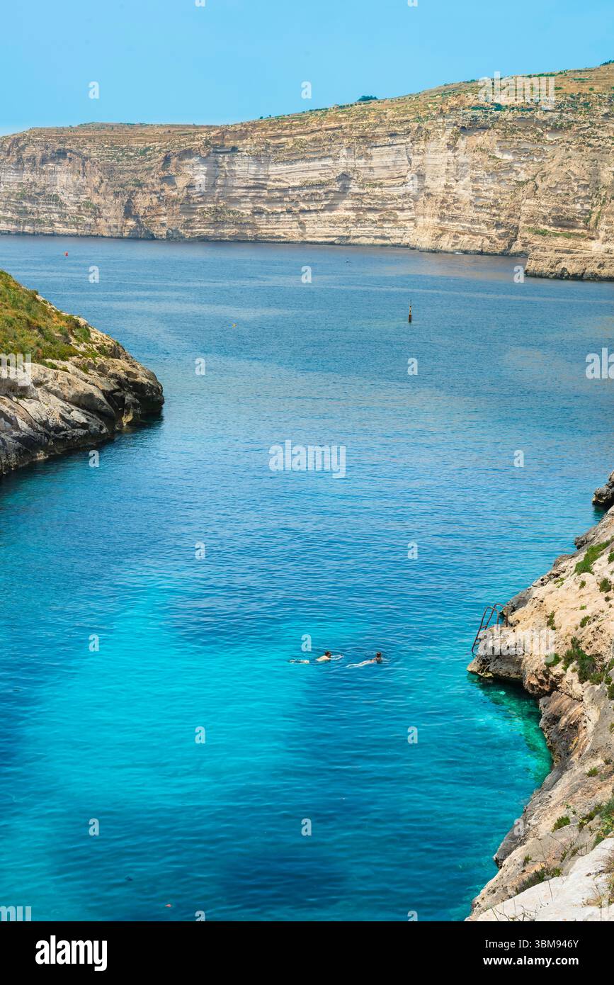 Costa di Gozo, vista in estate di due persone che nuotano in un'insenatura isolata conosciuta come Kantra Valley vicino alla baia di Xlendi, la costa meridionale di Gozo, Malta Foto Stock