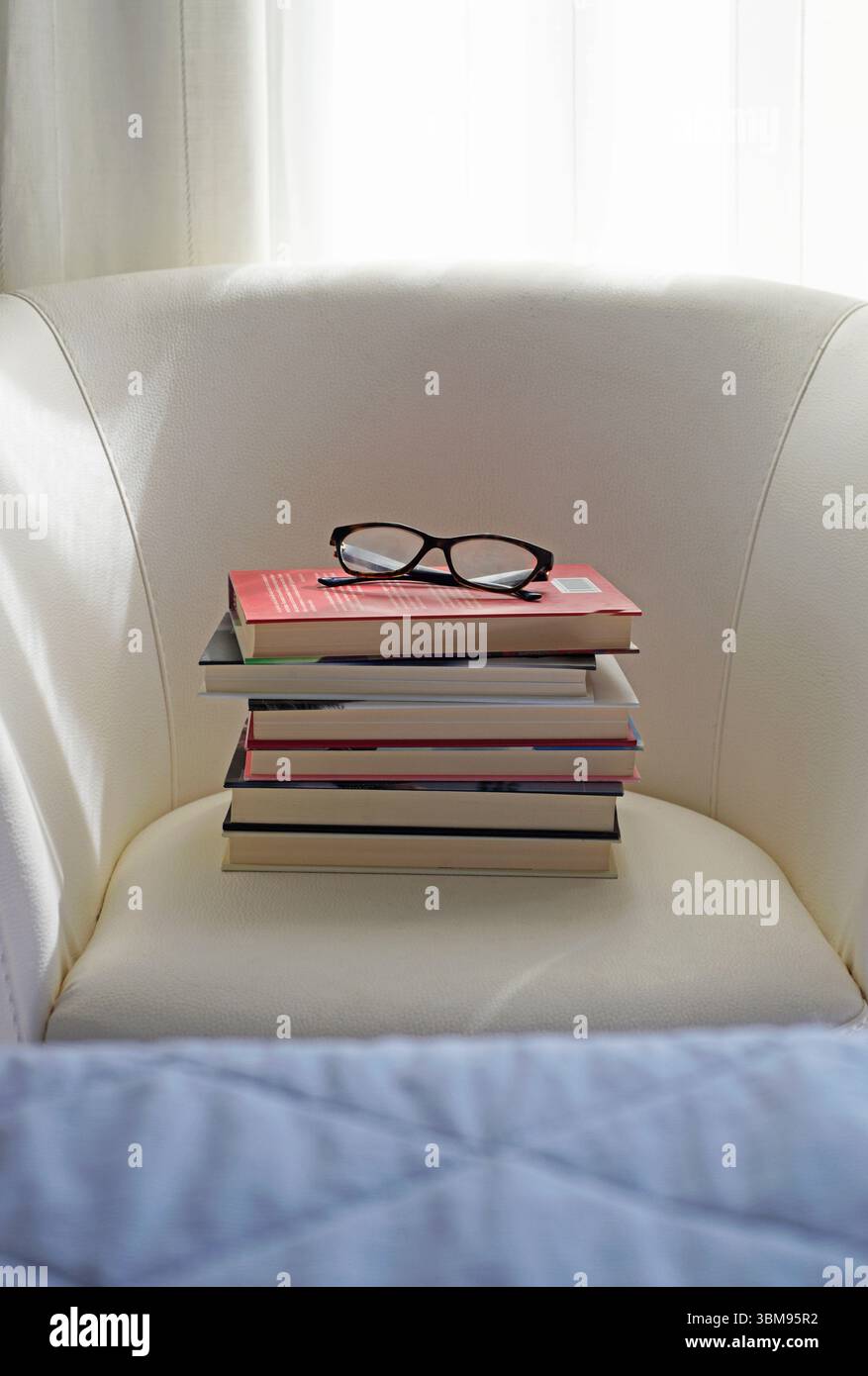 un mucchio di libri e occhiali da vista su una poltrona bianca Foto Stock