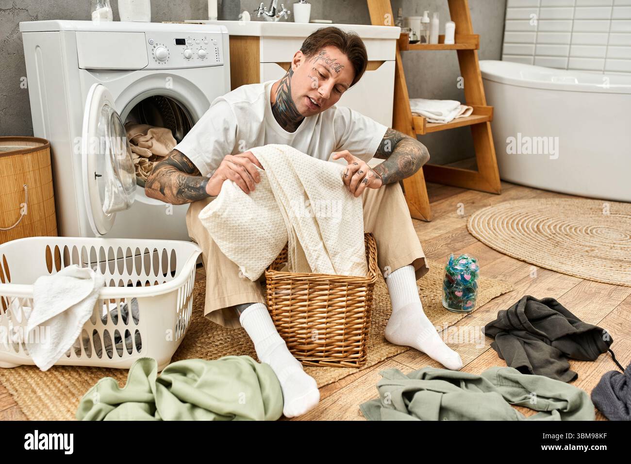 Un giovane uomo tatuato ordina il bucato a casa, irradiando calore e relax. Foto Stock