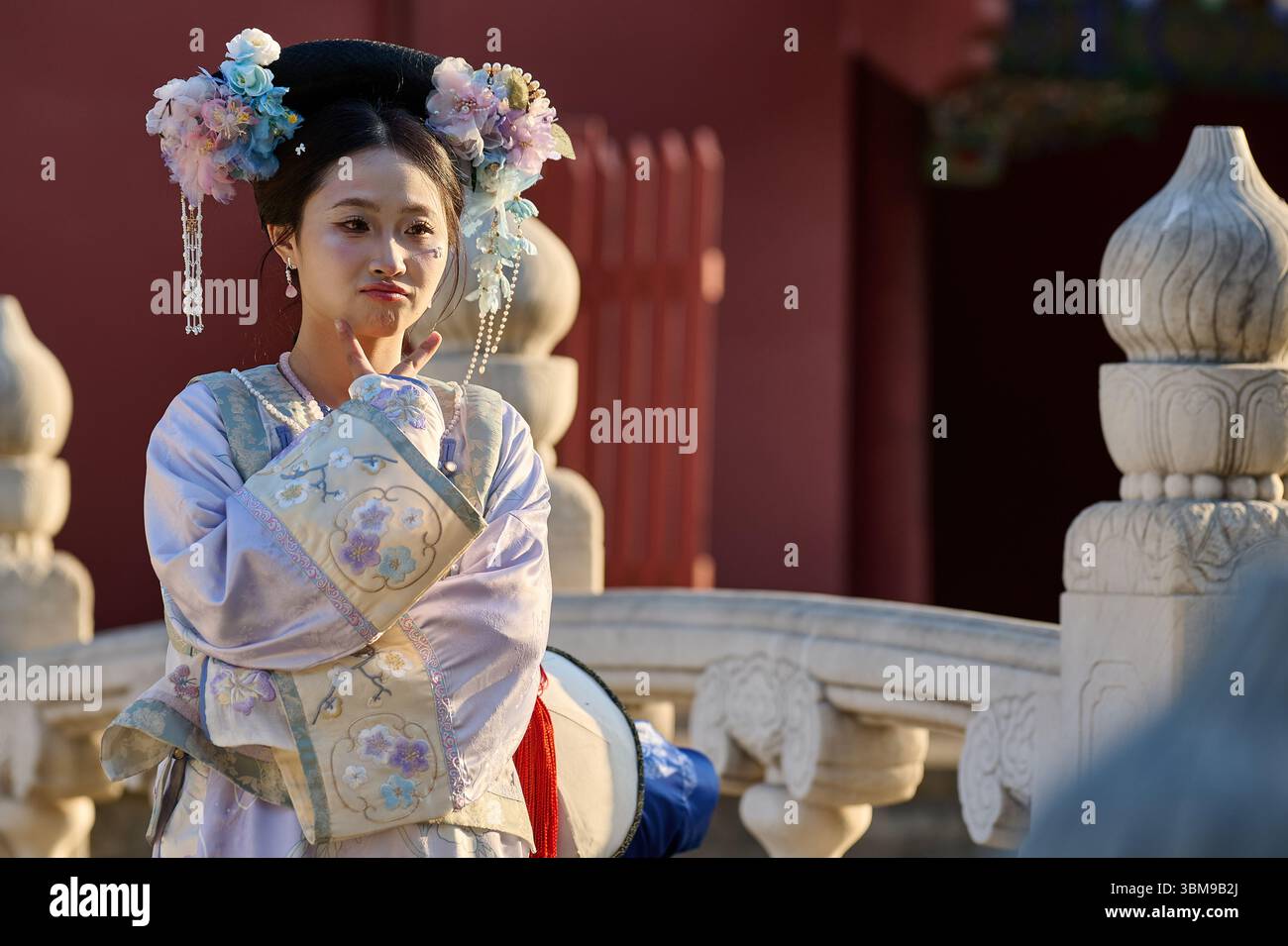 Donna in tradizionale abito cinese pastello che fa un gesto giocoso durante il servizio fotografico Foto Stock