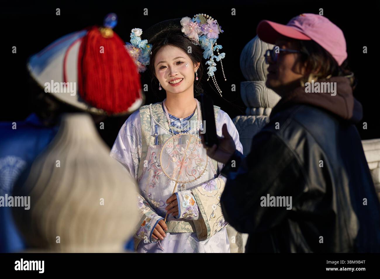 Donna in abito tradizionale cinese sorridente dietro un ventaglio di pizzi durante la sessione fotografica Foto Stock