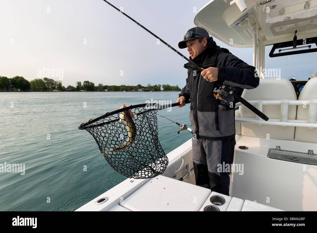 Pescatore su una barca che regge una rete con un pesce che ha catturato Foto Stock