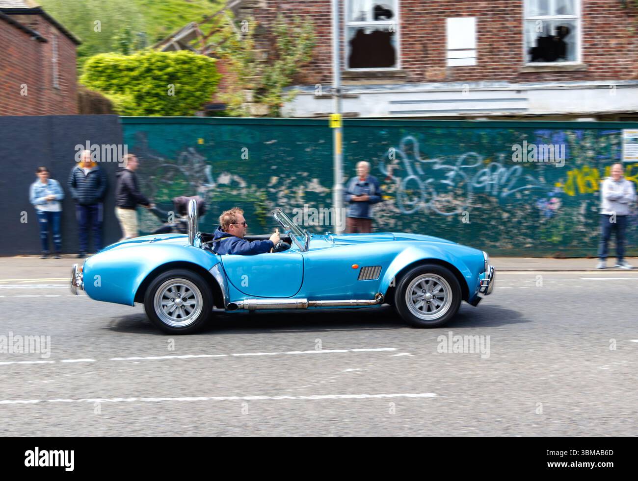 Una classica divisa sportiva decappottabile AC Cobra blu passa davanti a pareti ricoperte di graffiti con persone che guardano a Morpeth northumberland Foto Stock
