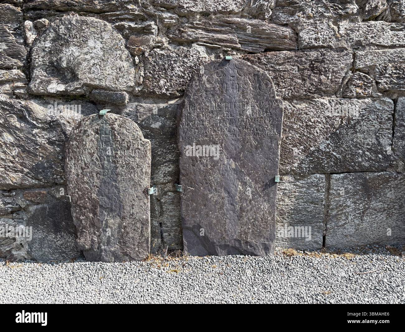 Antiche lapidi di pietra si stagliano contro un muro di roccia a Glendalough, contea di Wicklow, Irlanda, vicino alle rovine storiche della cattedrale. Foto Stock