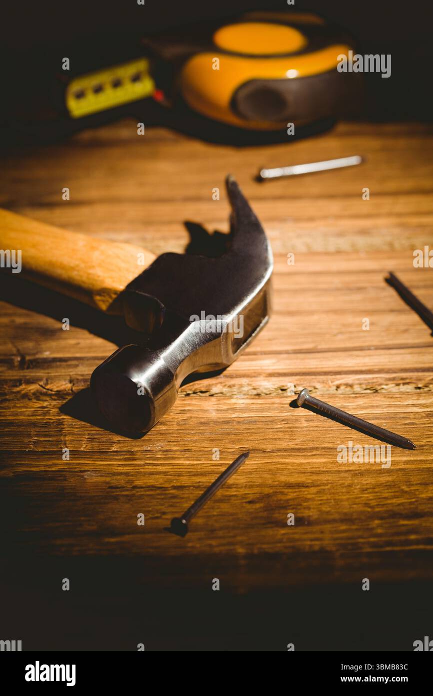 Il martello a baionetta poggia su un banco di lavoro in legno, con design piatto che mostra chiodi sparsi e metro a nastro Foto Stock