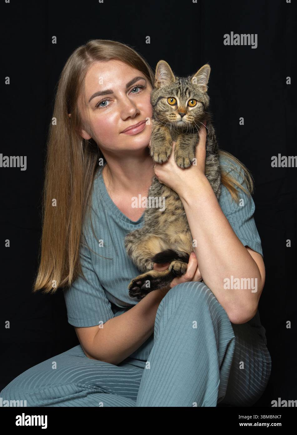Ritratto di una giovane donna che tiene delicatamente il gattino a righe su un solido sfondo nero. Ideale per temi di amore, cura, adozione, salvataggio degli animali e com Foto Stock