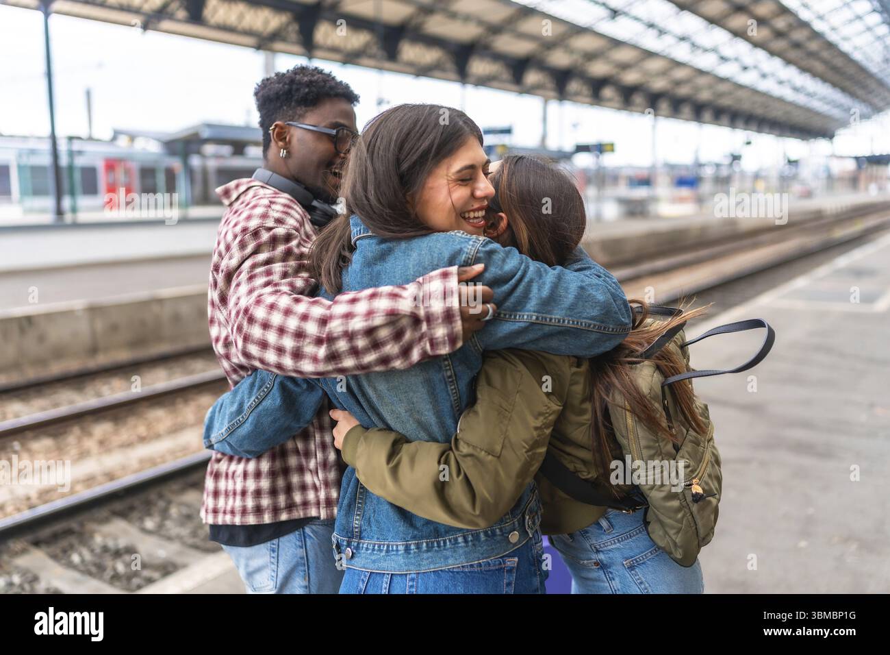 Tre studenti felici che si abbracciano alla stazione ferroviaria, emozionati per il loro viaggio o felici di incontrarsi di nuovo Foto Stock