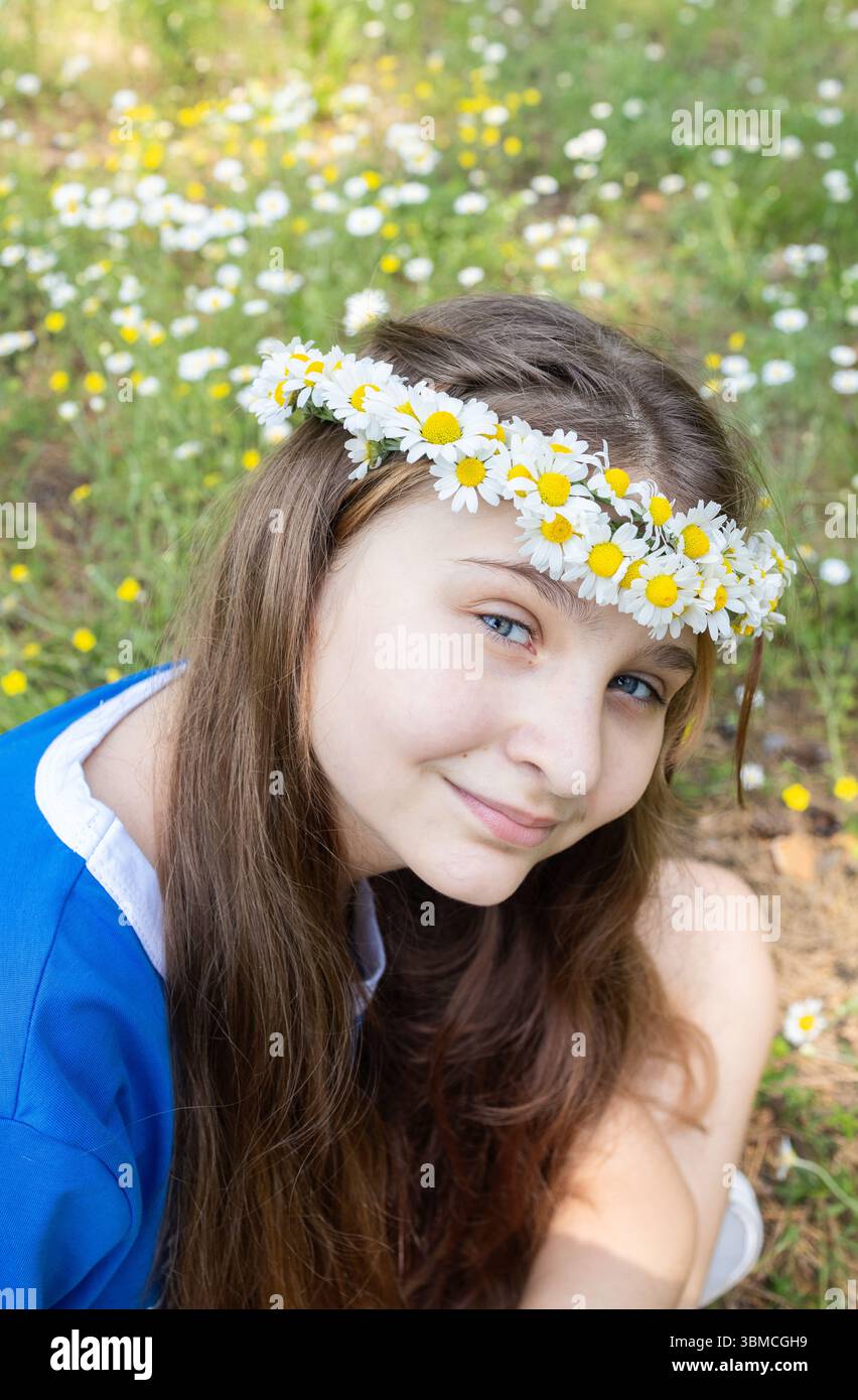 Ritratto di una ragazza sorridente di 12 anni in una cortina intrecciata di margherite nel parco. Godetevi il momento, siate positivi. Estate gioiosa. Gioie adolescenti Foto Stock