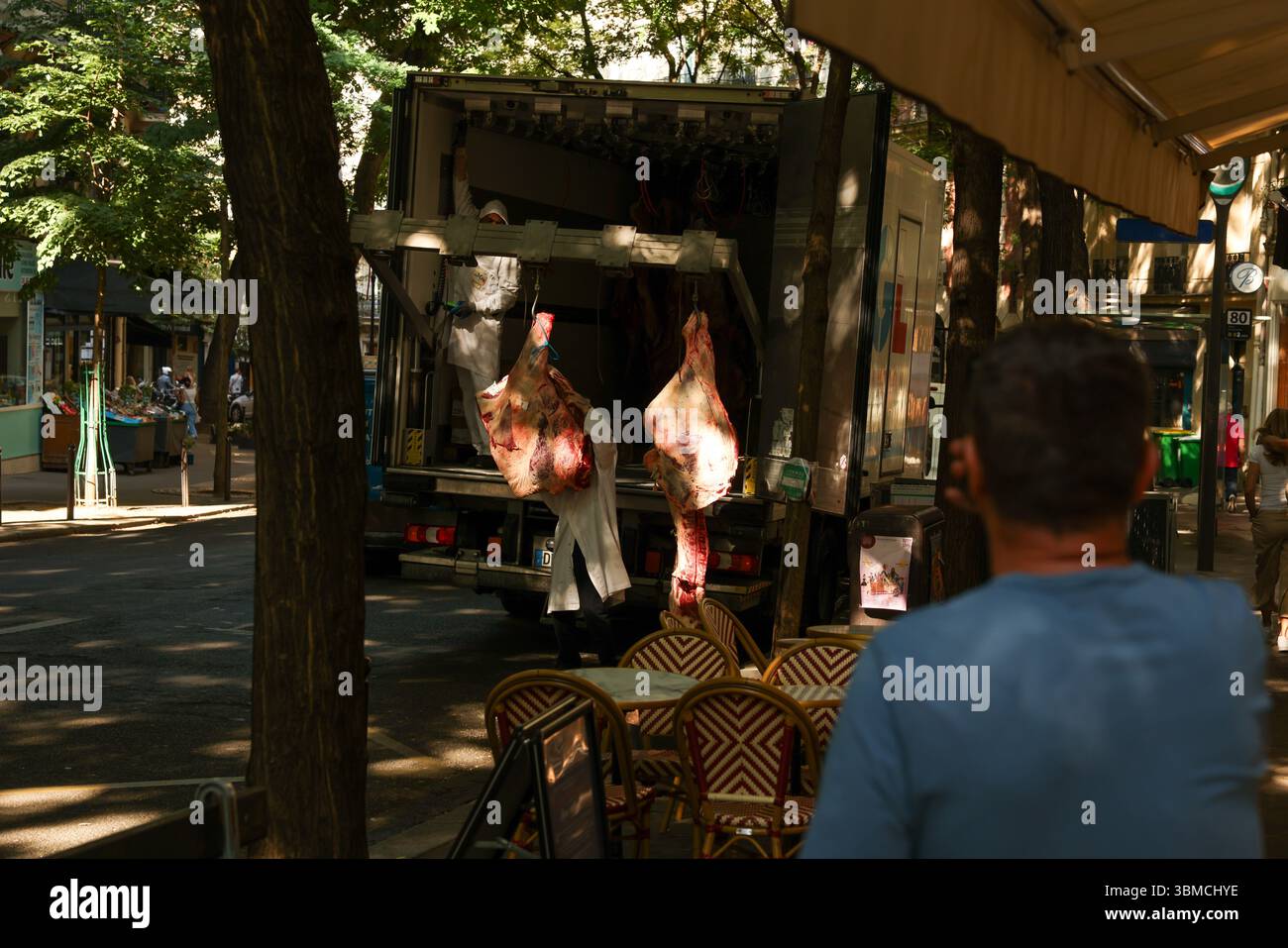 Due macellai in cappotti bianchi scaricano grandi lati di manzo da un camion refrigerato parcheggiato in una soleggiata strada parigina. Foto Stock