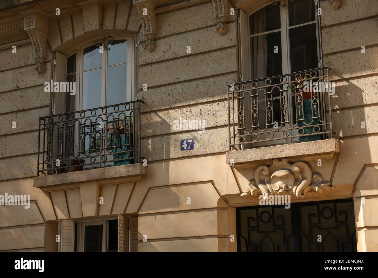 Un dettaglio ravvicinato della facciata di un edificio di appartamenti parigino, che presenta due balconi con ringhiere di ferro ornate, piante in vaso ed elegante vittoria Foto Stock