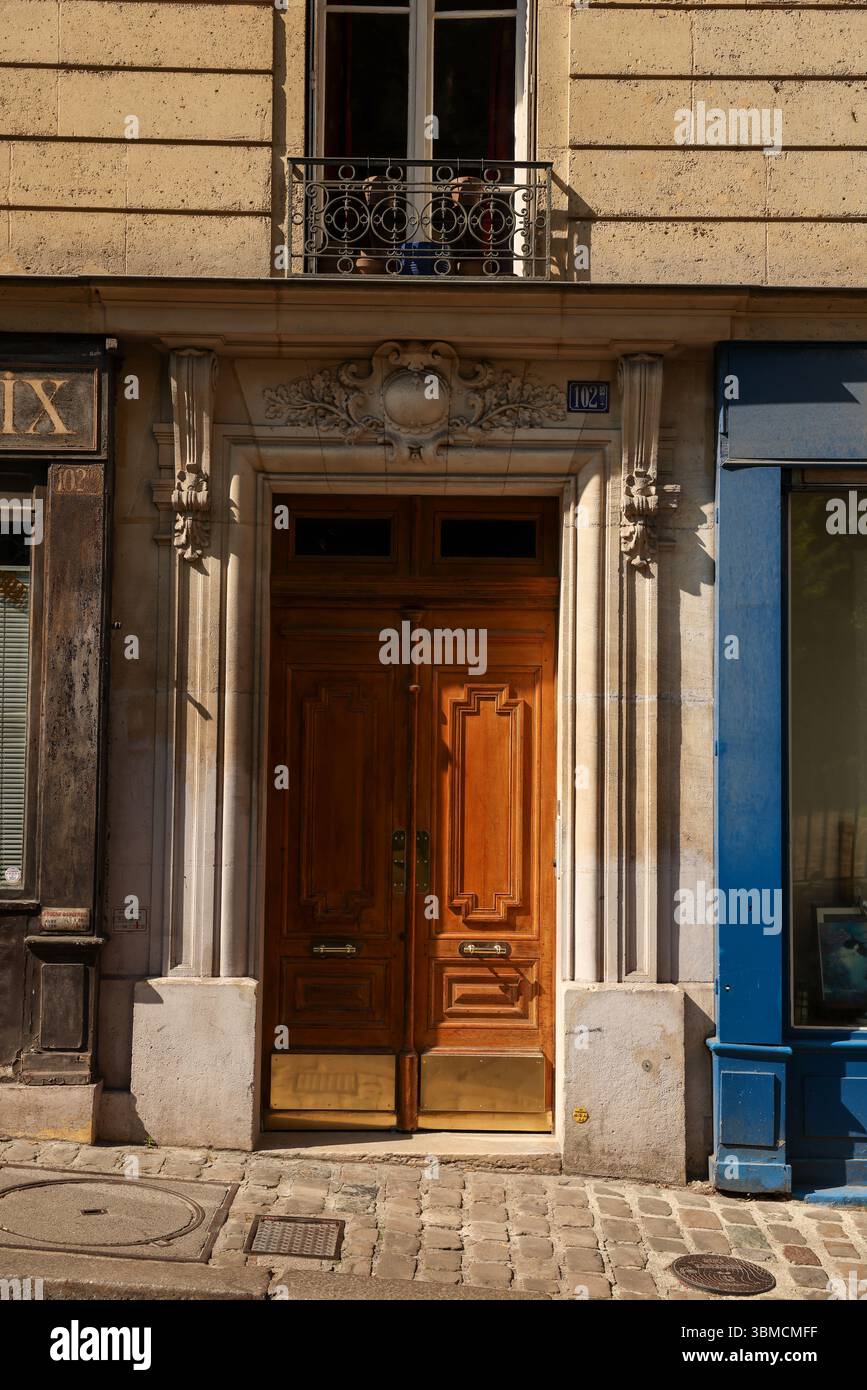 Una fotografia di un classico edificio parigino caratterizzato da una doppia porta in legno marrone ornata accentuata da ottone. La facciata dell'edificio è in pietra beige Foto Stock