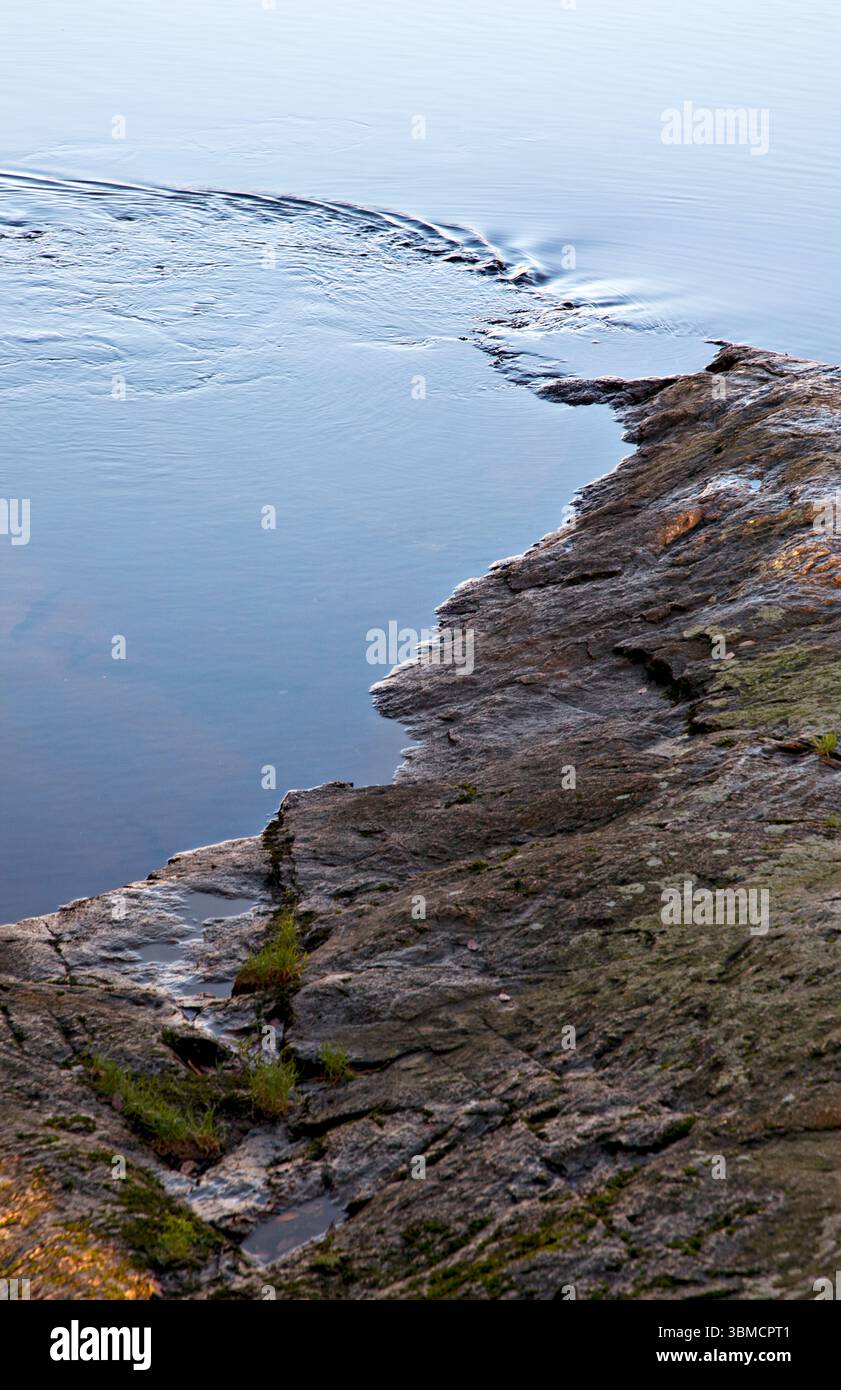 L'acqua si ripete dalla fine di una roccia sul bordo delle acque. Llyn Padarn Snowdonia, Gwynedd, Galles Regno Unito Foto Stock