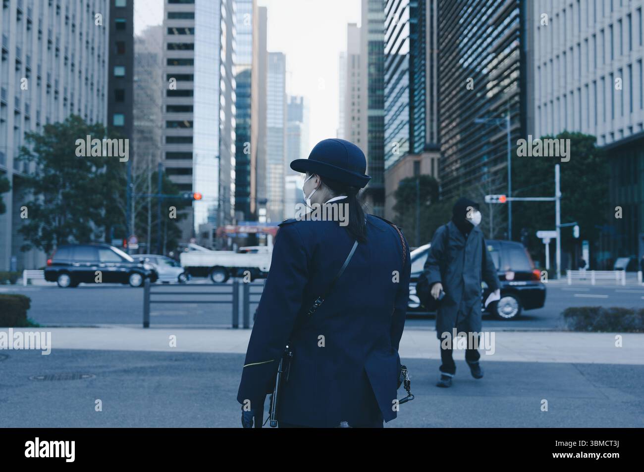 Un agente di sicurezza in uniforme con un cappotto blu si trova ad un incrocio nel centro di Tokyo Foto Stock