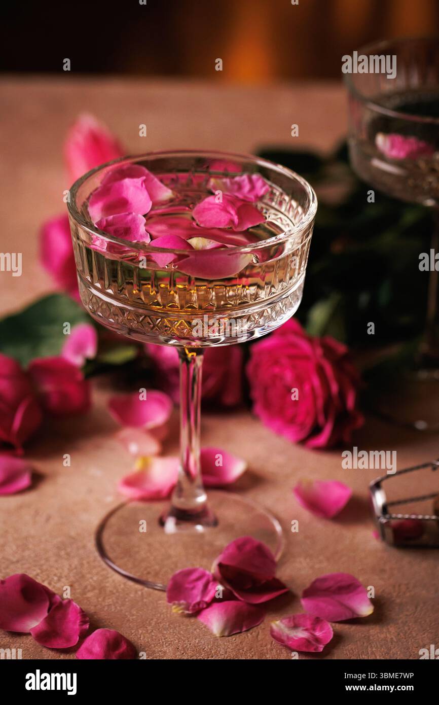 Bicchiere di champagne con petali di rosa e decorazioni romantiche Foto Stock